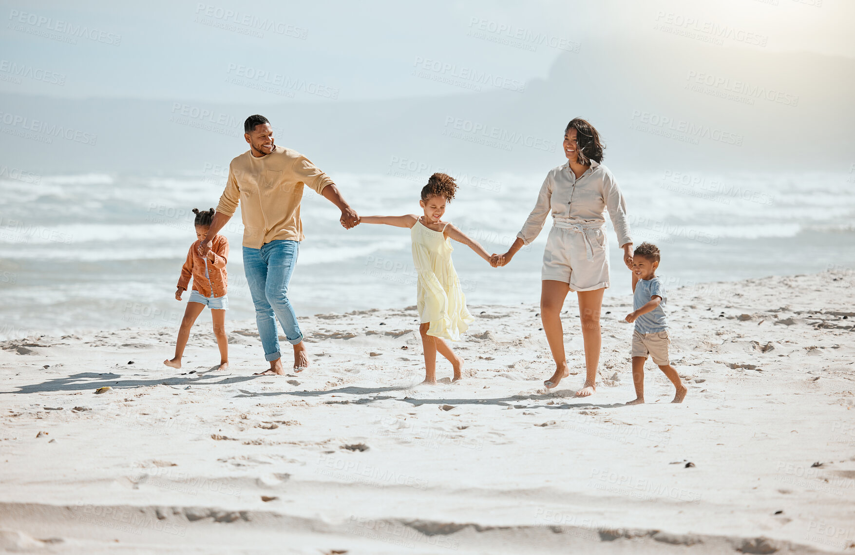 Buy stock photo Happy mixed race family with three children holding hands and walking along the beach together. Loving parents with two daughters and son having fun and spending time while on vacation