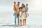 Portrait of a cheerful mixed race family with three children standing together at the beach and smiling while looking at the camera. Loving parents with their two daughters and son enjoying holiday by the beach