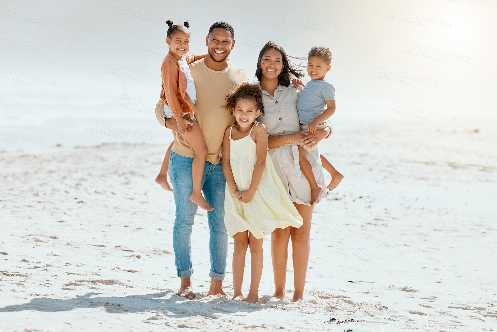 Buy stock photo Portrait of a cheerful mixed race family with three children standing together at the beach and smiling while looking at the camera. Loving parents with their two daughters and son enjoying holiday by the beach