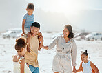 Happy mixed race family with three children laughing and talking while walking along the beach together. Loving parents with two daughters and son having fun and spending time while on vacation