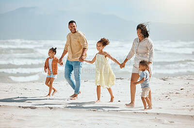 Happy mixed race family with three children holding hands and walking along the beach together. Loving parents with two daughters and son having fun and spending time while on vacation