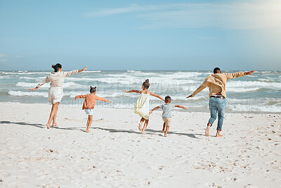 Playful mixed race family with three children running on the beach with arms outstretched. A big family spending time and enjoying holiday by the sea