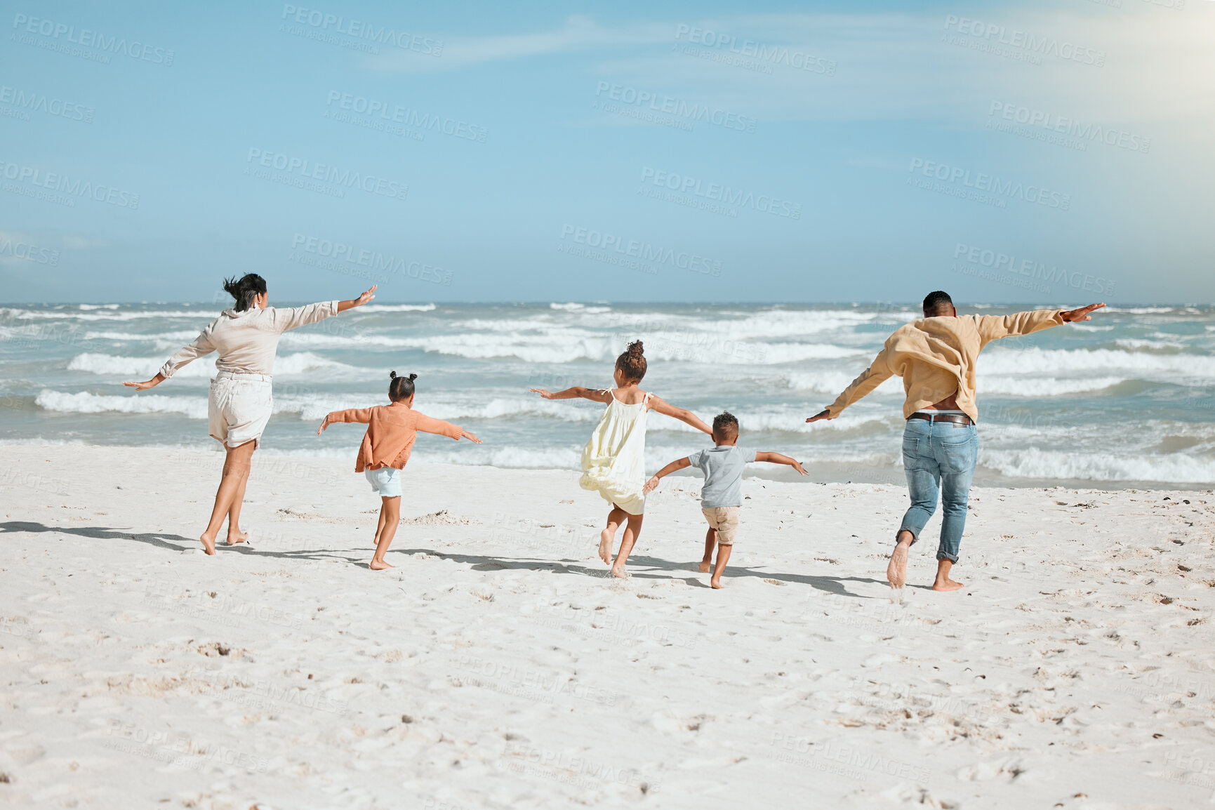 Buy stock photo Playful mixed race family with three children running on the beach with arms outstretched. A big family spending time and enjoying holiday by the sea