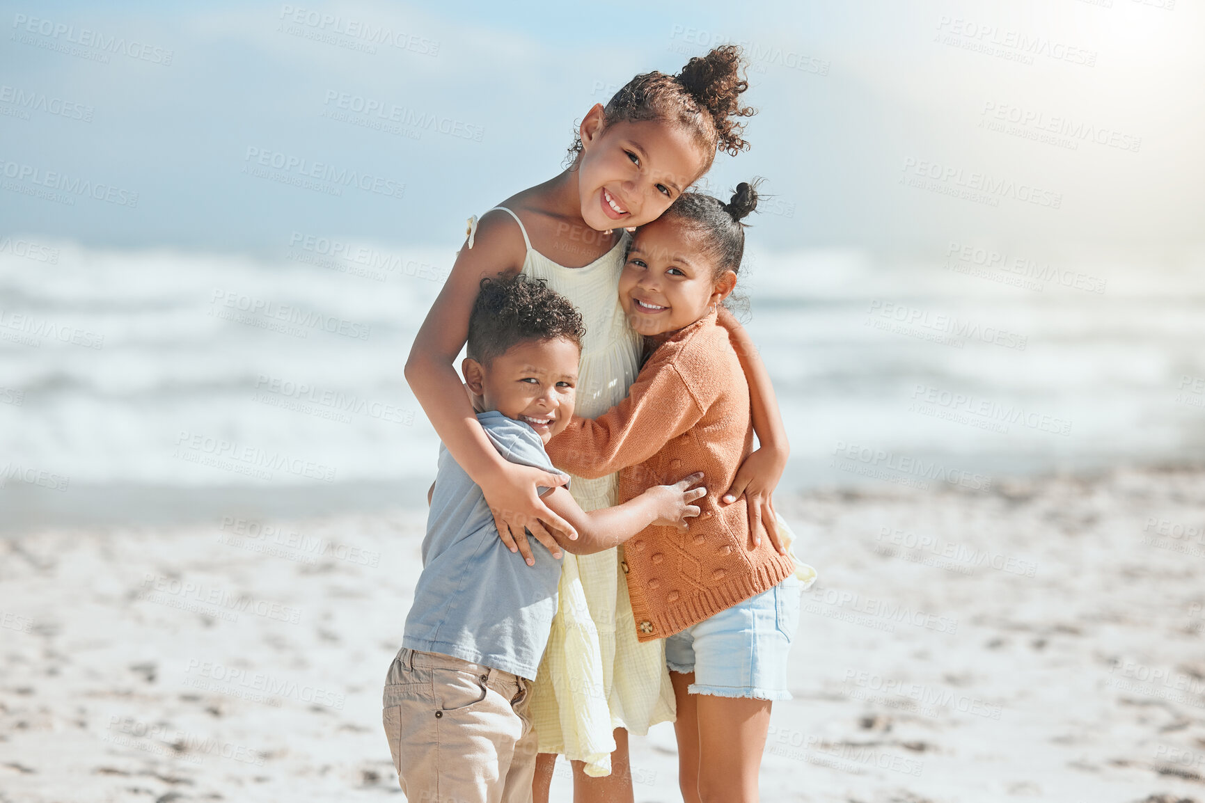 Buy stock photo Adorable little girl hugging and embracing her two younger siblings at the beach. Big sister showing her little brother and sister love and affection