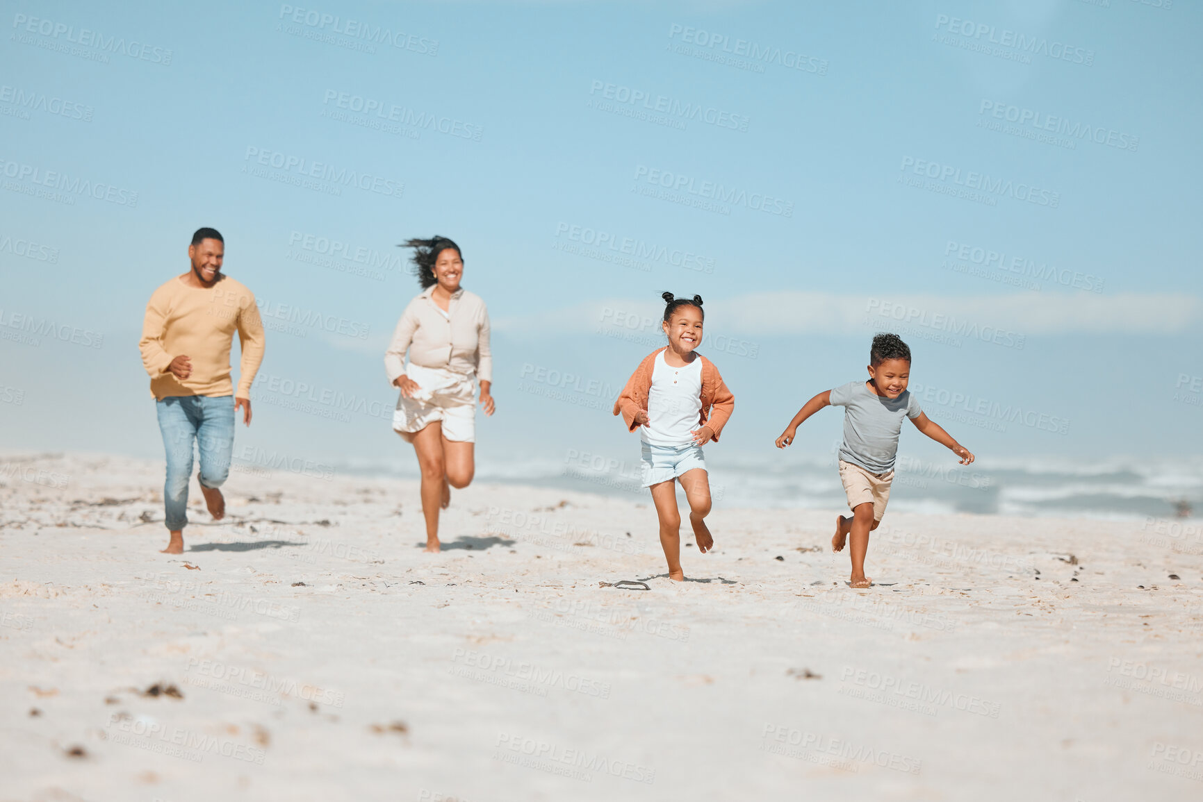 Buy stock photo Cheerful young mixed race family running on the beach, Happy mother and father with two children having fun during summer holiday. Playful casual family racing on sandy beach enjoying time together