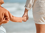 Close up of little girl holding mothers hand while standing on the beach. Mother and daughter holding hands and watching waves crash by the sea