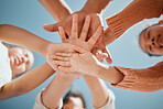 View from below of young mixed race family stacking their hands on top of each other while standing together against a blue sky. Parents and children showing unity and trust