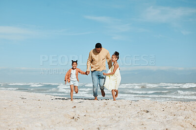 Cheerful young mixed race father running on the beach with his two daughters. Two energetic little girls enjoying day at the beach while on holiday with their dad