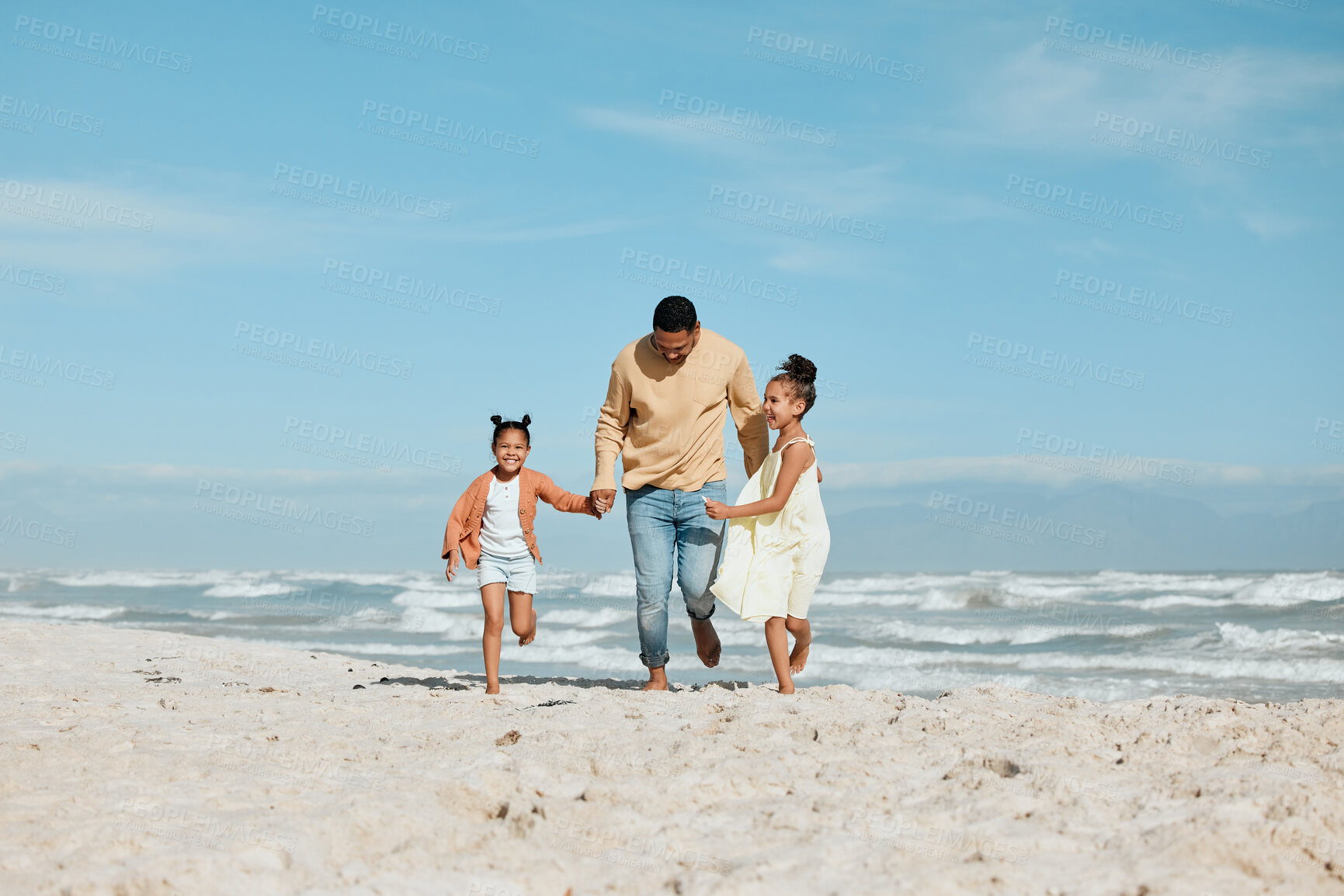 Buy stock photo Cheerful young mixed race father running on the beach with his two daughters. Two energetic little girls enjoying day at the beach while on holiday with their dad