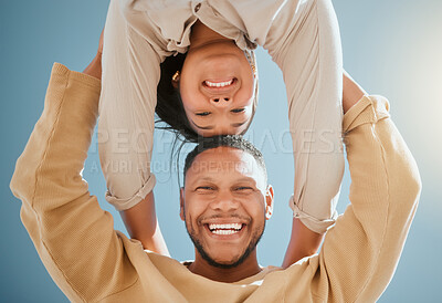 Buy stock photo Happy young mixed race couple standing with their hands on each other others shoulders while looking down and smiling at the camera against a blue sky, from below