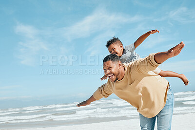 Cheerful young mixed race father being playful while giving his son a piggyback ride on his back and stretching out their arms pretending to fly. Energetic dad and little boy having fun and spending time together while on vacation by the beach
