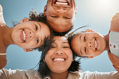 Buy stock photo Portrait of a happy young mixed race family standing together in huddle smiling and looking down at camera on a sunny day. Faces of cheerful parents and two daughters embracing each other from below