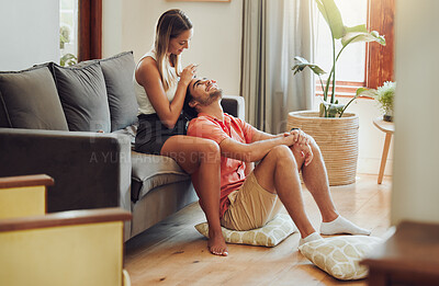Buy stock photo Loving young caucasian couple sitting together at home spending time and happy to be together. Happy young woman sitting on couch while her boyfriend sits between her legs as she plays with his hair and gently massages his head