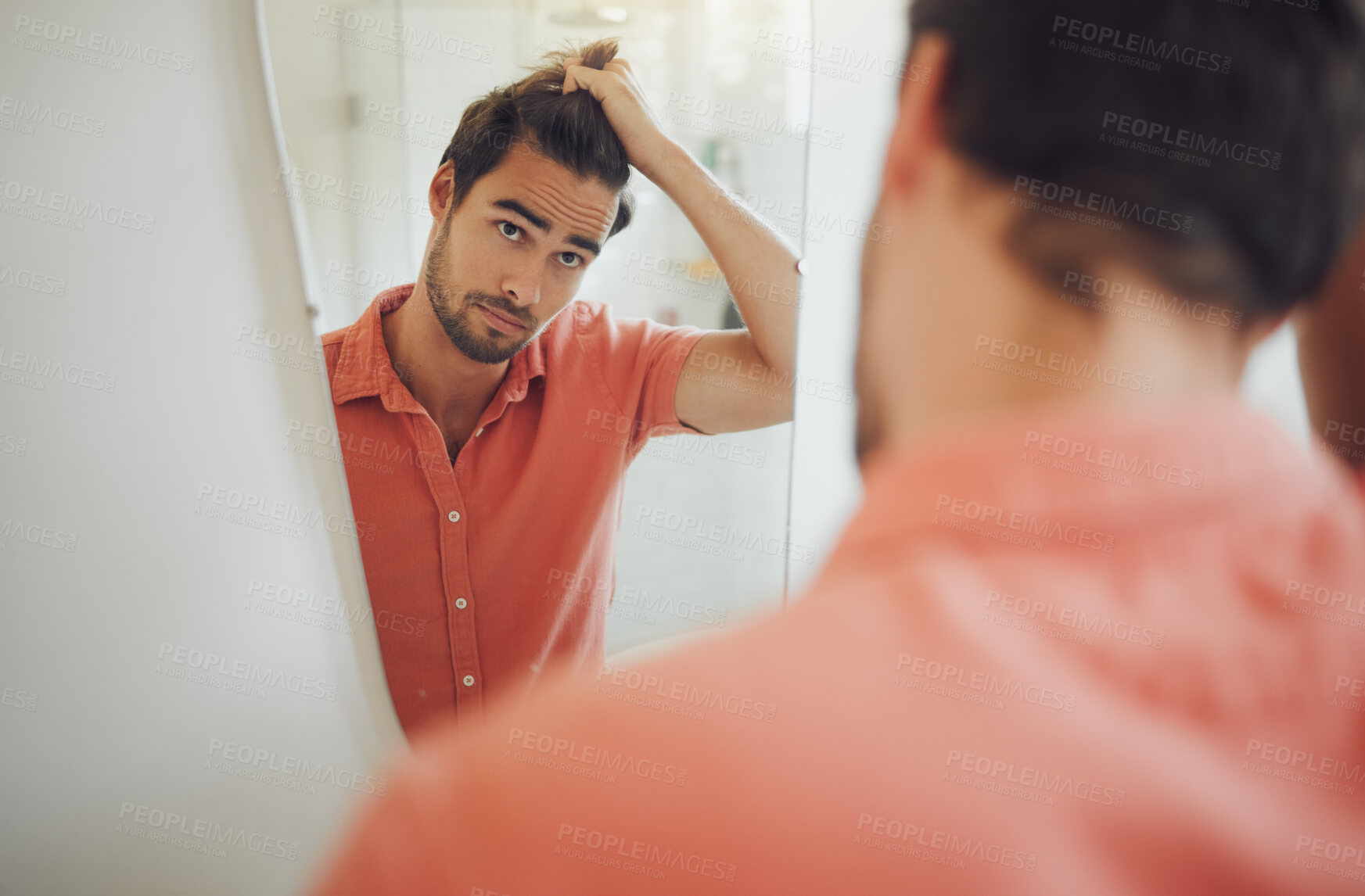 Buy stock photo Handsome young caucasian man touching his hair and looking in the bathroom mirror. Male pulling his hair and thinking of getting a haircut. Concerned man worried about dandruff, receding hairline or hair loss