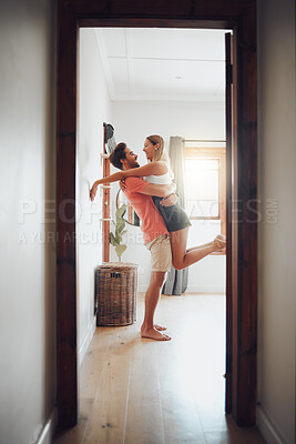 Buy stock photo Joyful young man holding his girlfriend in arms as he lifts her up while they look into each others eyes and share intimate moment. Romantic young couple hugging and enjoying passionate dance at home
