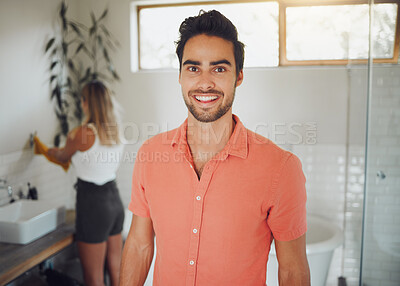 Buy stock photo Portrait of a young caucasian couple sharing a bathroom with focus on happy young man smiling showing perfect teeth while looking at the camera in the foreground. Girlfriend washing hands in background