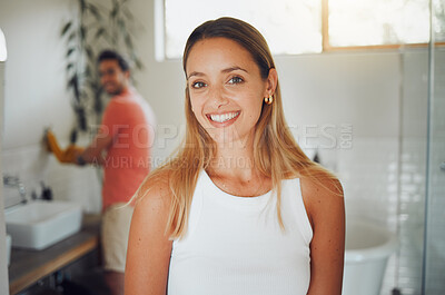 Buy stock photo Young caucasian couple sharing a bathroom with focus on happy young woman smiling while looking at the camera in the foreground while waiting to get ready. Boyfriend washing hands in background