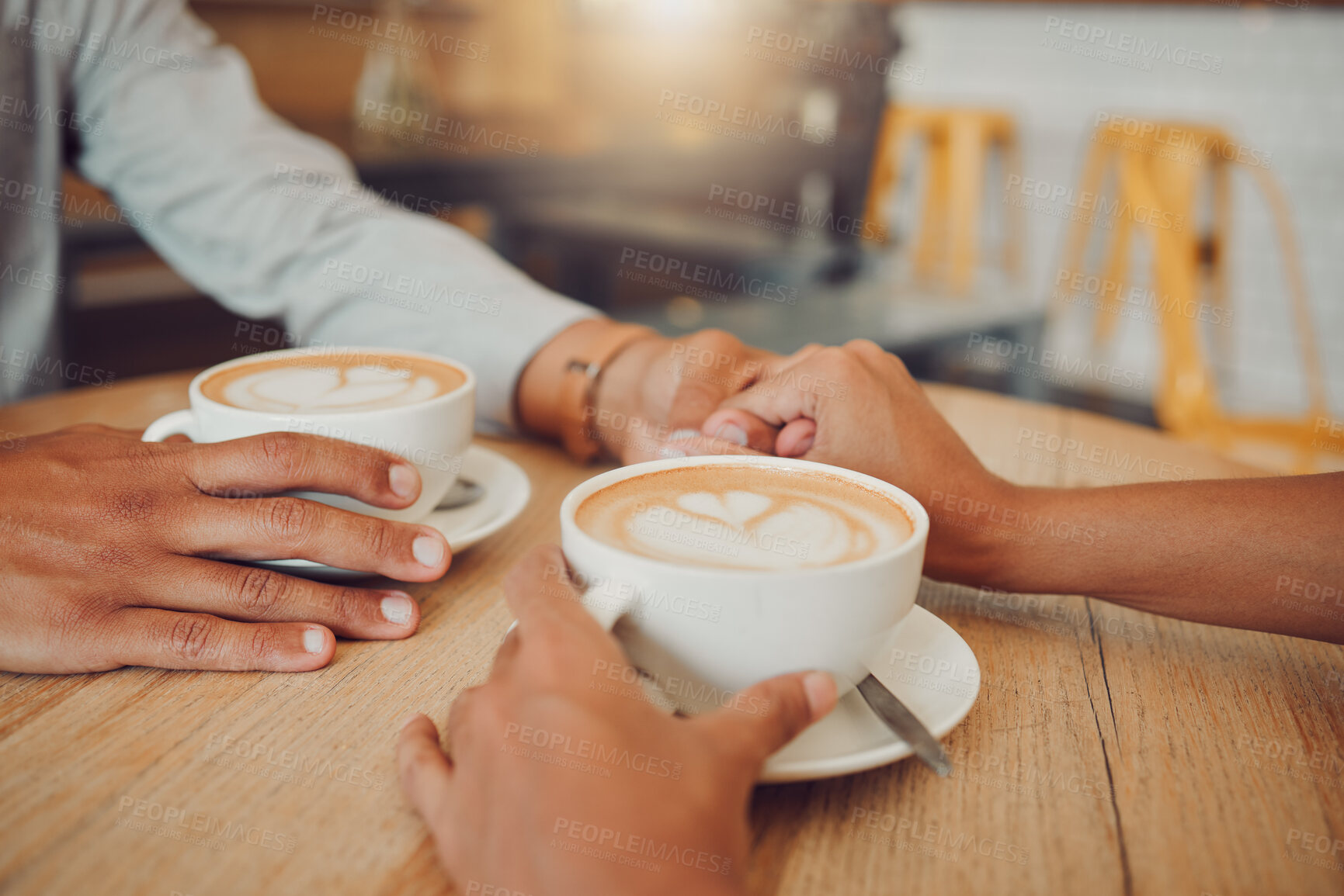 Buy stock photo Close up of young couple in love holding hands with two cups of coffee on a table while sitting in a cafe. Male and female hands with hot cappuccino or espresso  while on a date in a restaurant