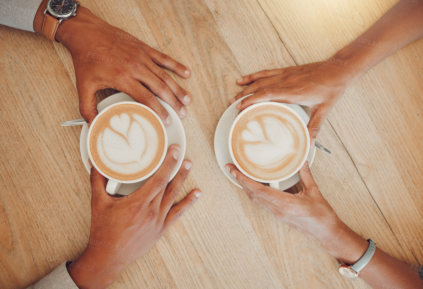 Buy stock photo Close up of young couple holding cups of coffee on a wooden table while sitting in a cafe. Male and female hands with foamy hot cappuccino or espresso while on a date in a restaurant