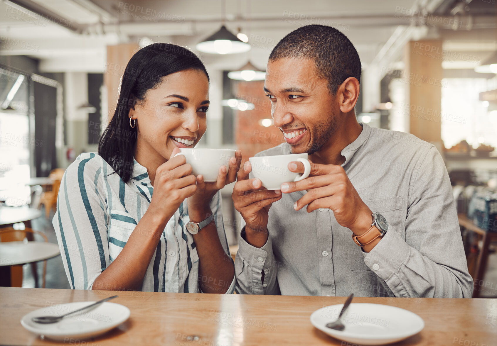 Buy stock photo Loving mixed race couple in love looking at each other while holding cups enjoying coffee in a cafe. Happy young woman and man on their first date in a restaurant
