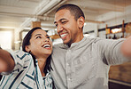 Loving young couple looking at each other and smiling while holding mobile phone to take a selfie in a cafe. Happy mixed race man and woman looking happy while sitting together on a date