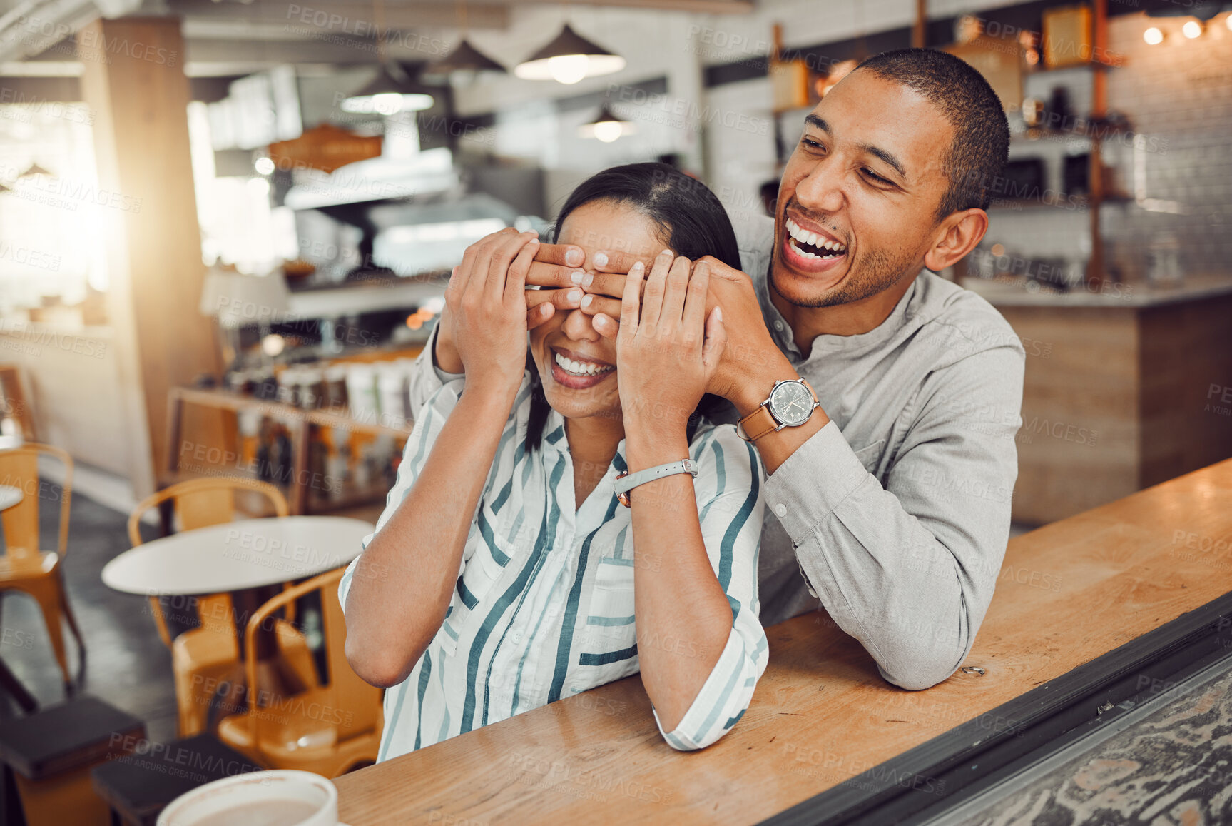 Buy stock photo Cheerful young man covering his girlfriends eyes and surprising her while sitting in a cafe. Happy young mixed race couple meeting for coffee on their first date. Excited woman trying to guess who is behind her