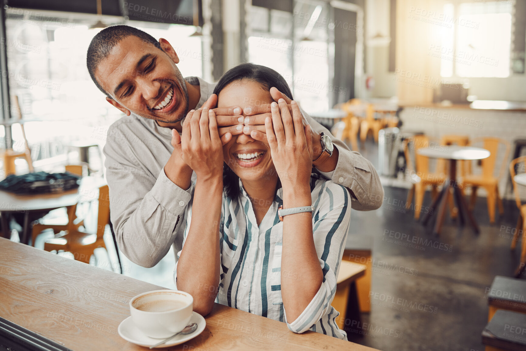 Buy stock photo Cheerful young man covering his girlfriends eyes and surprising her while sitting in a cafe. Happy young mixed race couple meeting for coffee on their first date. Excited woman trying to guess who is behind her