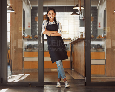 Proud businesswoman standing in the entrance of her coffeeshop. Portrait of happy small business owner standing in the door of her shop. Confident boss with her arms crossed in her restaurant
