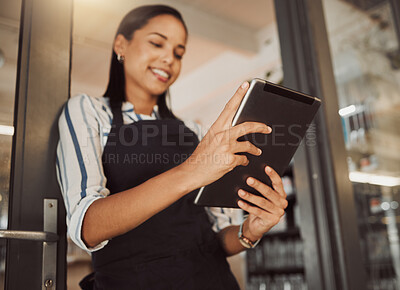 Businesswoman using a digital tablet in her shop entrance from below. Young business owner using a wireless device in her store entrance. Coffeeshop owner ordering stock for her store