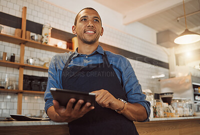 Barista dreaming while ordering stock on digital tablet. Mixed race businessman using wireless device in cafe kitchen. Business owner thinking while using online digital app.