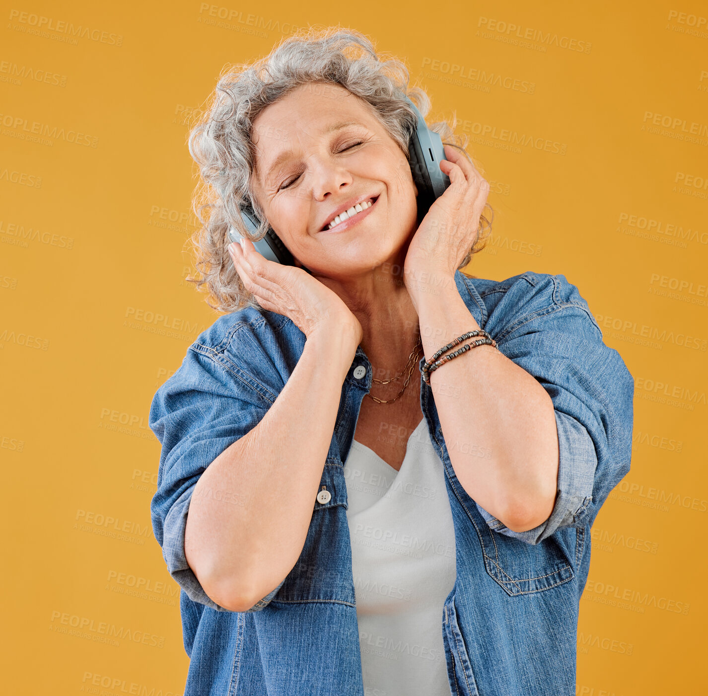 Buy stock photo One happy mature caucasian woman wearing headphones and listening to music while dancing against a yellow background in the studio. Smiling white woman feeling free while expressing through dance