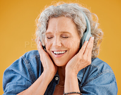 One happy mature caucasian woman wearing headphones and listening to music while dancing against a yellow background in the studio. Smiling white woman feeling free while expressing through dance