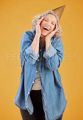 One happy mature caucasian woman wearing a birthday hat while posing against a yellow background in the studio. Smiling white lady celebrating another year while looking surprised and overjoyed