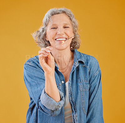 One happy mature caucasian woman playing with a sparkler on her birthday while posing against a yellow background in the studio. Smiling white lady showing joy and happiness while celebrating