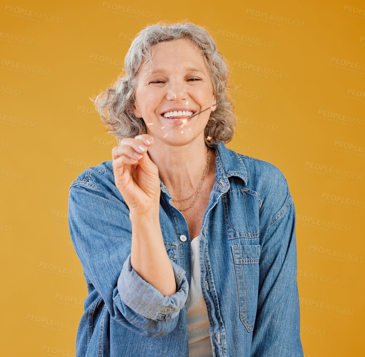 Buy stock photo One happy mature caucasian woman playing with a sparkler on her birthday while posing against a yellow background in the studio. Smiling white lady showing joy and happiness while celebrating