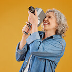 One happy caucasian woman standing against a yellow background in a studio and taking a picture on a camera. Confident cheerful caucasian lady holding a camera and taking a photograph. Smile and pose