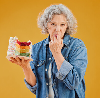 One happy mature caucasian woman holding a colourful cake with a slice missing against a yellow background in the studio. Smiling white lady showing joy and happiness while celebrating her birthday
