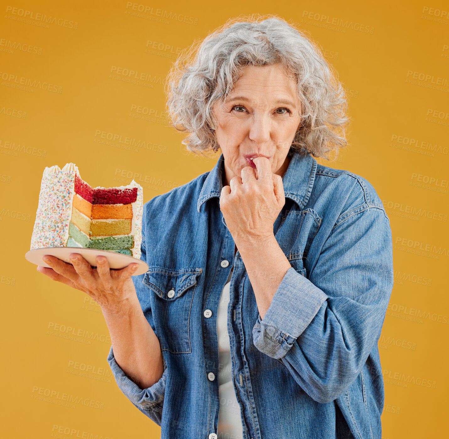 Buy stock photo One happy mature caucasian woman holding a colourful cake with a slice missing against a yellow background in the studio. Smiling white lady showing joy and happiness while celebrating her birthday