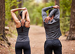 Rear view of young male and female athlete stretching before a run outside in nature. Two fit sportspeople doing warm-up exercises in pine forest on a sunny day