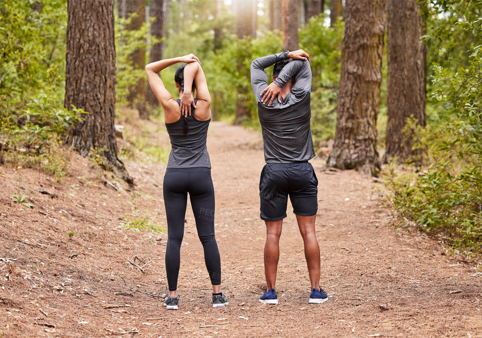 Buy stock photo Full length of a young male and female athlete stretching before a run outside in nature from behind. Two fit sportspeople doing warm-up exercises in pine forest on a sunny day