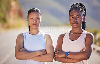 Portrait of two serious looking female athletes standing with their arms crossed while out for a run on a road. Two strong sportswomen exercising outdoors