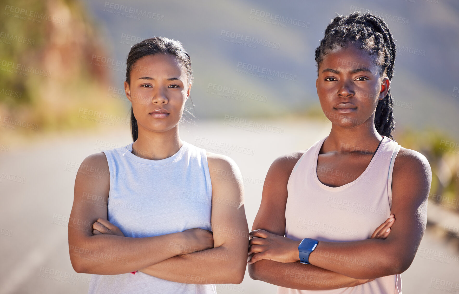 Buy stock photo Portrait of two serious looking female athletes standing with their arms crossed while out for a run on a road. Two strong sportswomen exercising outdoors