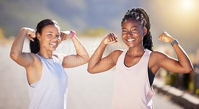 Buy stock photo Portrait of two happy young female athletes showing arm muscles while out for a run on a road. Two strong sportswomen posing together after training