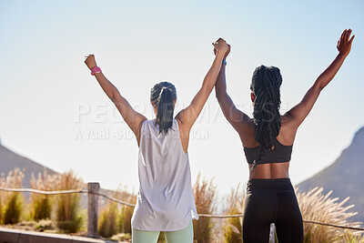 Buy stock photo Rear view of two fit young sportswomen standing with their hands raised in the air together celebrating their victory after achieving fitness goals together. Two female athletes raising their arms up after exercising outdoors