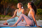 Full length of yoga women bonding and sitting together on mats after outdoor practice in remote nature. Two beautiful young active smiling friends at sunset. Happy people after being mindful and zen