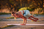 Full length yoga woman holding side crow pose in outdoor practice in remote nature. One beautiful caucasian fit person using mat, balancing on hands while stretching alone at sunset, active, healthy