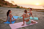 Full length of yoga women bonding, sitting together on mats after outdoor practice in remote nature. Diverse group of young active smiling friends at sunset. Three happy people being mindful and zen