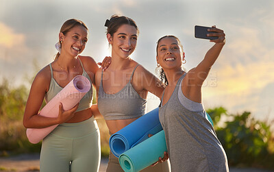 Buy stock photo Beautiful yoga women using a cellphone to take selfies while holding yoga mats in outdoor practice in remote nature. Diverse group of young smiling active friends standing together. Three happy people