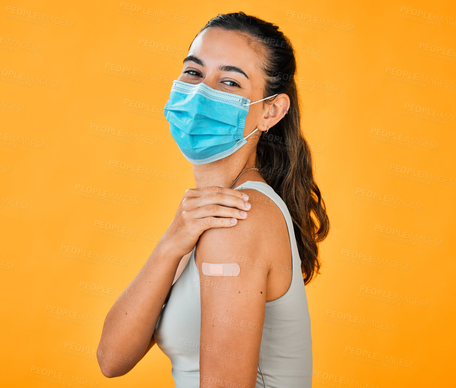 Buy stock photo Mixed race covid vaccinated woman showing plaster on arm, wearing surgical face mask. Portrait of hispanic woman isolated against yellow studio background with copyspace. Protected with corona vaccine