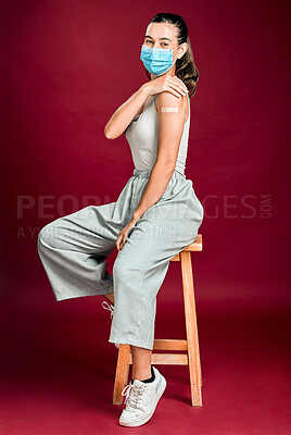 Mixed race covid vaccinated woman showing plaster on arm, wearing surgical face mask. Full length portrait of hispanic woman isolated against red background in studio with copyspace. Corona vaccine